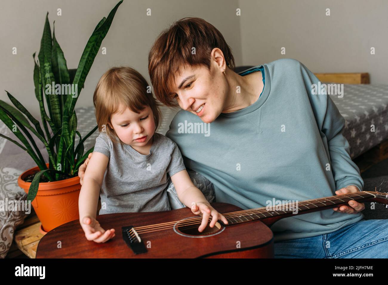 Une petite fille joue de la guitare avec sa mère sur le sol à la maison Banque D'Images