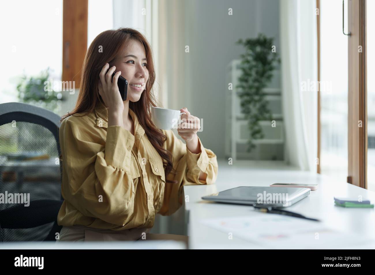 Communication d'entreprise. Femme d'affaires asiatique parlant sur un téléphone mobile travaillant sur un ordinateur portable dans un bureau moderne. Banque D'Images