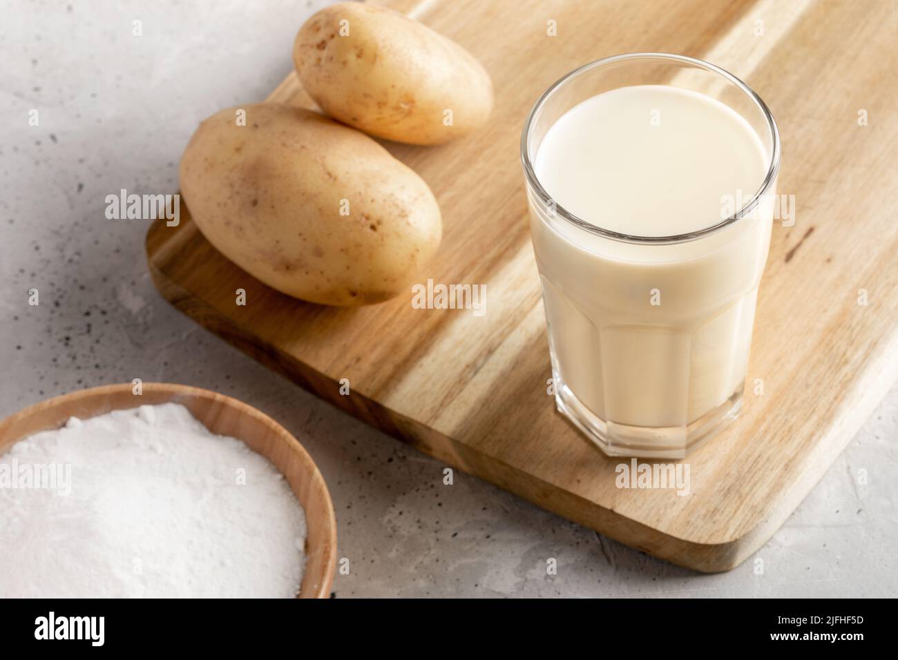 Verre de lait de pomme de terre végétalien en poudre gros plan, poudre de pomme de terre et tubercules sur fond de béton. Lait de remplacement non laitier. Outil de remplacement du lait de légumes. Sélection Banque D'Images