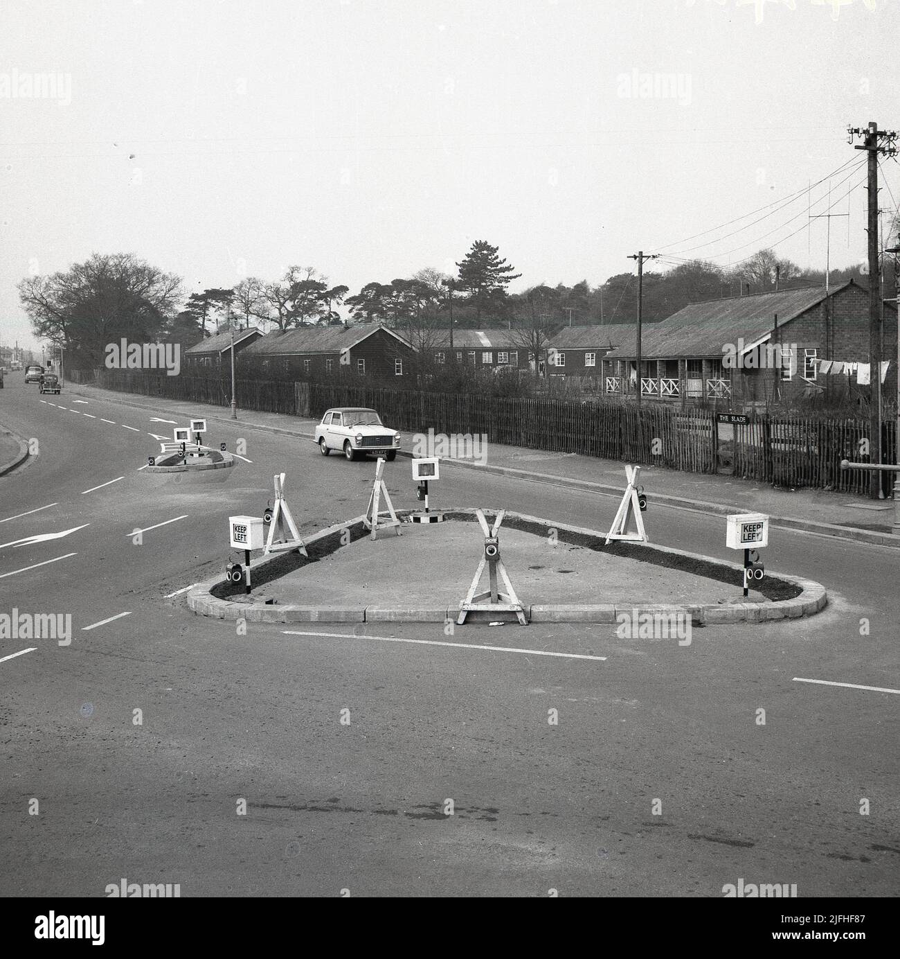 1960s, historique, une voiture Austin A40 de l'époque approchant d'une nouvelle route ou carrefour sur Slade Rd, Oxford, Angleterre, Royaume-Uni. L'image de droite montre les anciens camps de l'armée au large de la Slade, qui ont fourni des logements très nécessaires aux familles dans la période d'après-guerre. Banque D'Images