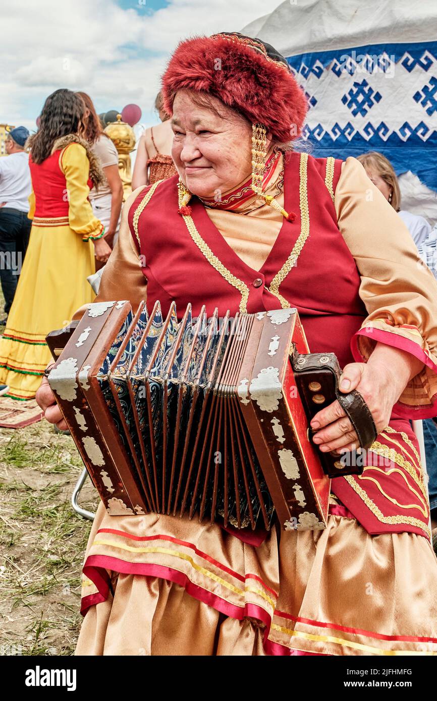 Femme âgée en vêtements de fête traditionnels Bashkir jouant de l'accordéon national à Sabantuy Holiday Banque D'Images