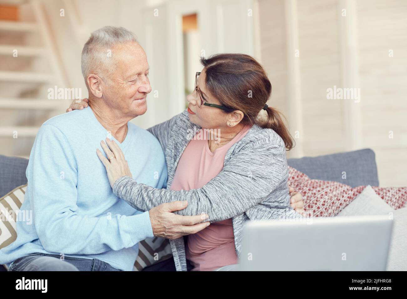 Inquiète femme sénior aimante assise sur un canapé et embrassant son mari tout en lui posant des questions sur la santé Banque D'Images