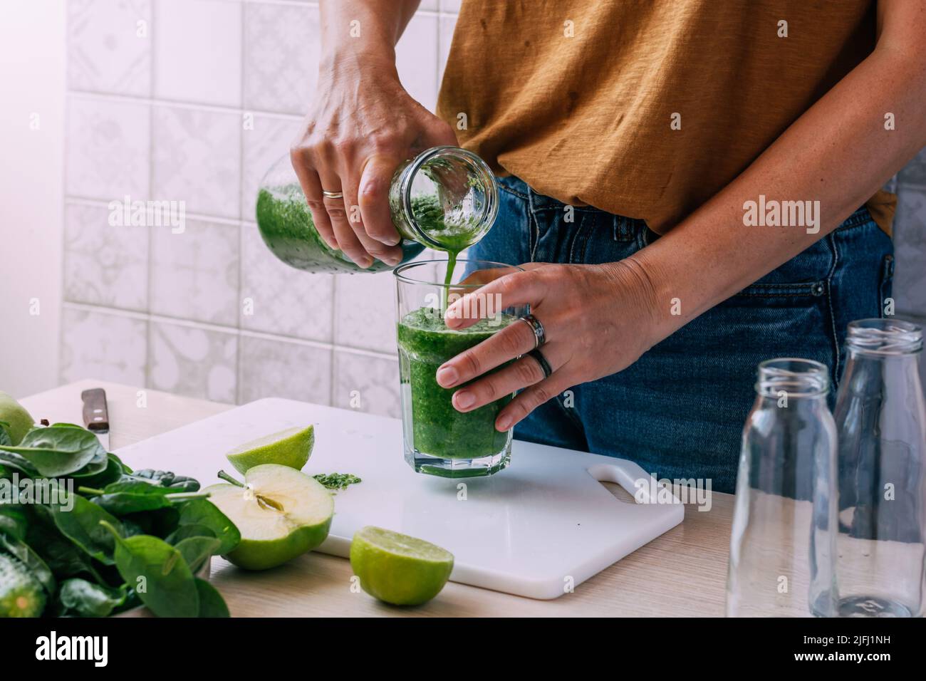 Une femme verse un smoothie fraîchement préparé à partir de légumes verts et de fruits dans le verre. Végétarisme Banque D'Images