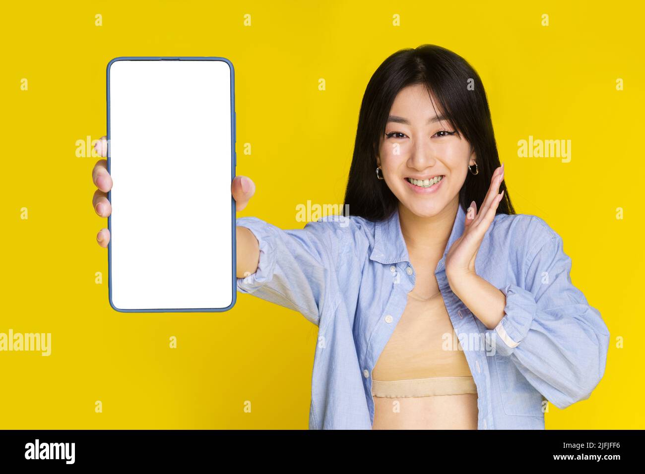 Émerveillement jeune fille asiatique montrant ou présentant téléphone mobile blanc écran blanc et sourire excité sur l'appareil photo isolé sur fond jaune. Fille utilisant un smartphone. Accent sélectif sur la fille. Banque D'Images