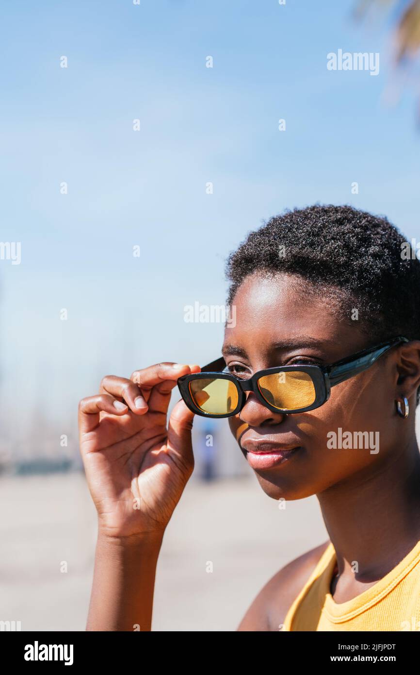 portrait vertical d'une femme afro-américaine attrayante en retirant des lunettes de soleil jaunes tendance Banque D'Images