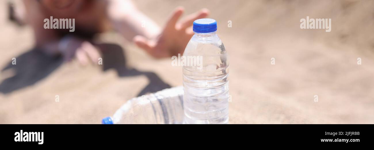 Un homme dans le désert s'étire sur le sable pour des bouteilles d'eau Banque D'Images