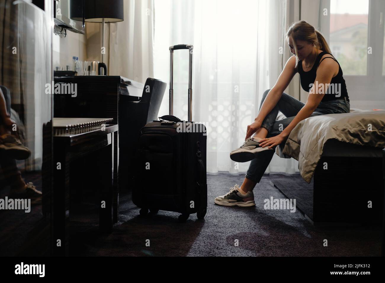 femme prenant des chaussures dans une chambre d'hôtel ensoleillée sur le lit. Touriste se détendre dans la chambre d'hôtel après avoir voyagé avec une valise. Bonne femme de se reposer Banque D'Images