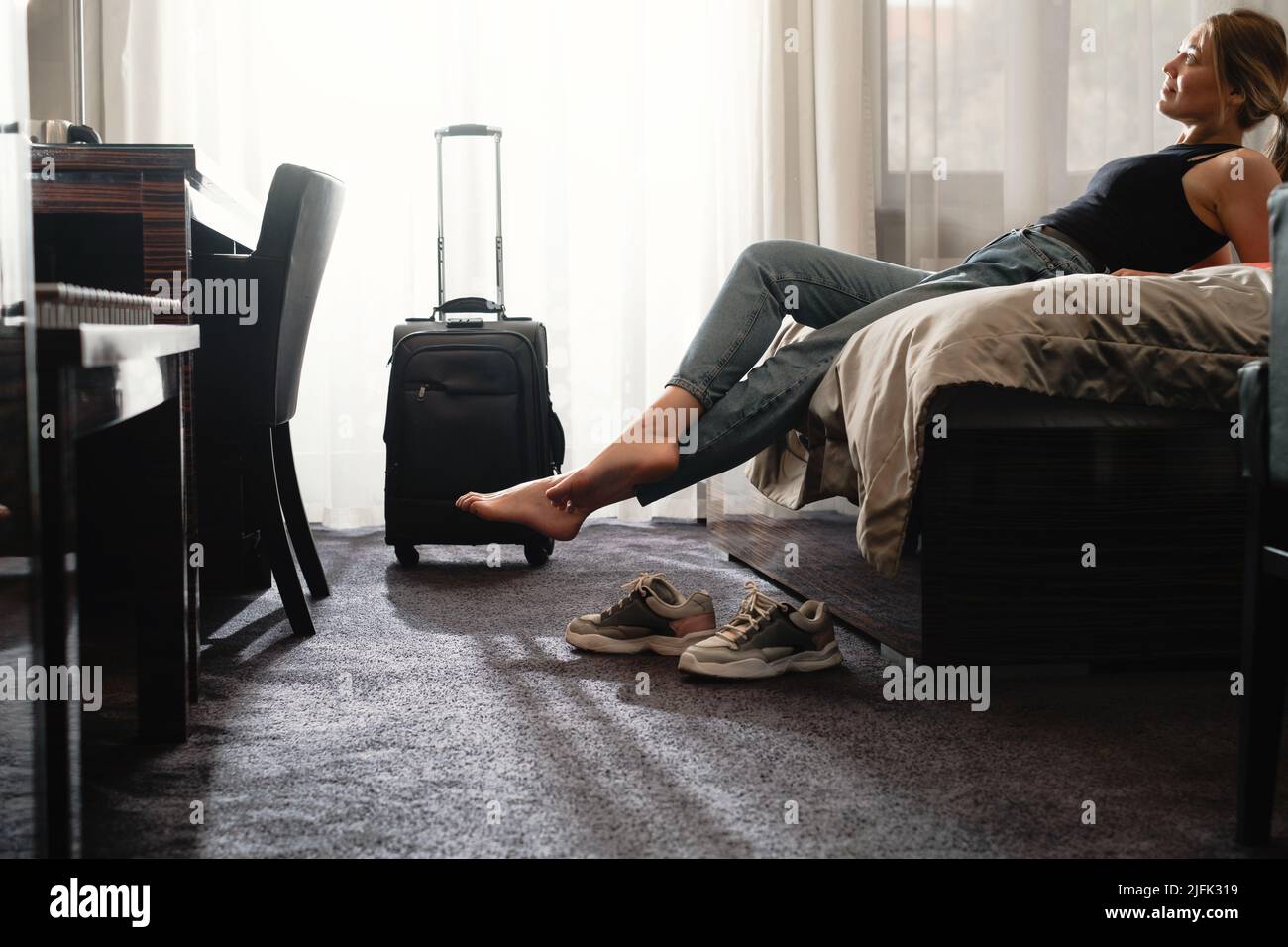 femme prenant des chaussures dans une chambre d'hôtel ensoleillée sur le lit. Touriste se détendre dans la chambre d'hôtel après avoir voyagé avec une valise. Bonne femme de se reposer Banque D'Images