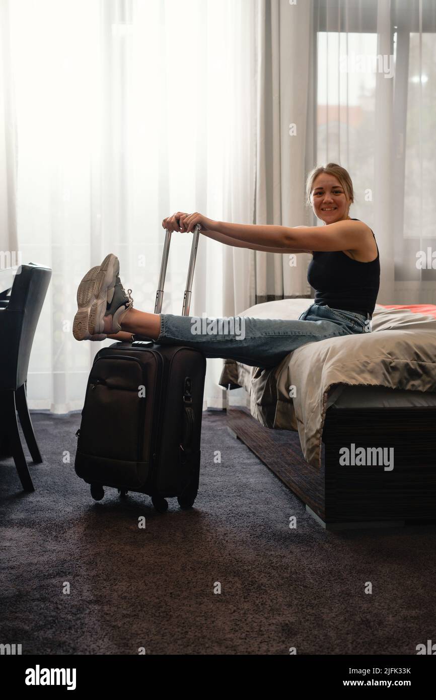 femme prenant des chaussures dans une chambre d'hôtel ensoleillée sur le lit. Touriste se détendre dans la chambre d'hôtel après avoir voyagé avec une valise. Bonne femme de se reposer Banque D'Images