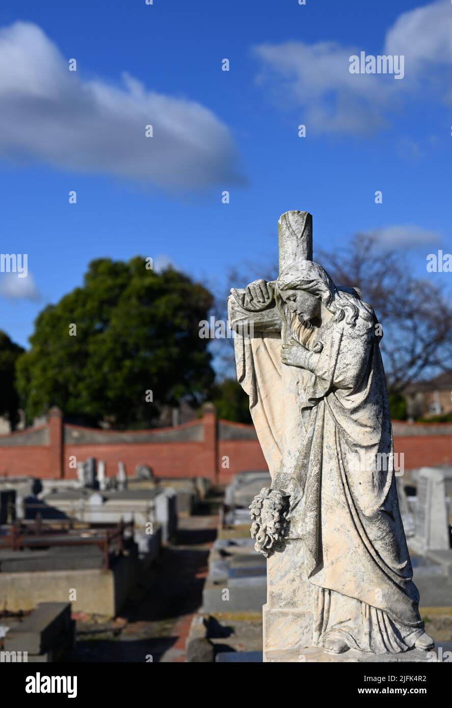 Sculpture en pierre usée d'une femme pleurant tout en s'appuyant sur une croix chrétienne, ou crucifix, avec des rangées de tombe en arrière-plan Banque D'Images