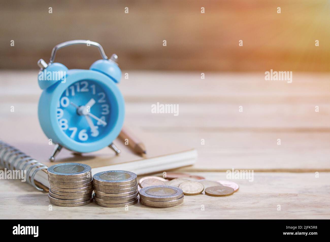 Pièces de monnaie, horloge en alram et crayon avec bloc-notes vide sur fond de table en bois. Bureau avec pièces de monnaie et concept de planification financière d'affaires Banque D'Images