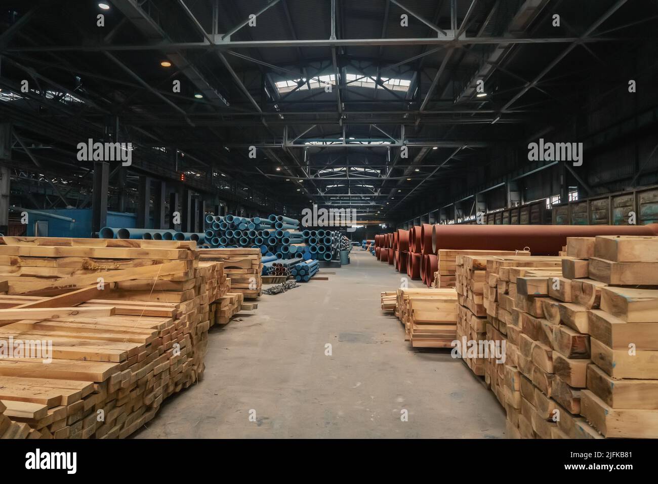 Grand entrepôt avec tuyaux d'eau et piles de bois en usine. Banque D'Images