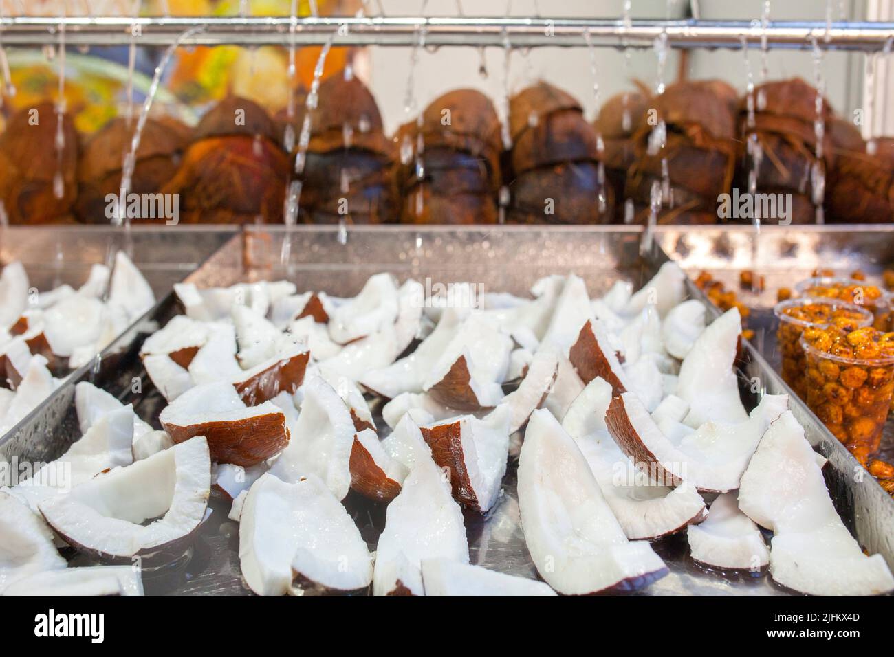 Tranches de noix de coco fraîches. Des gouttes d'eau tombent sur des pièces exposées au stand du marché de la rue. Banque D'Images