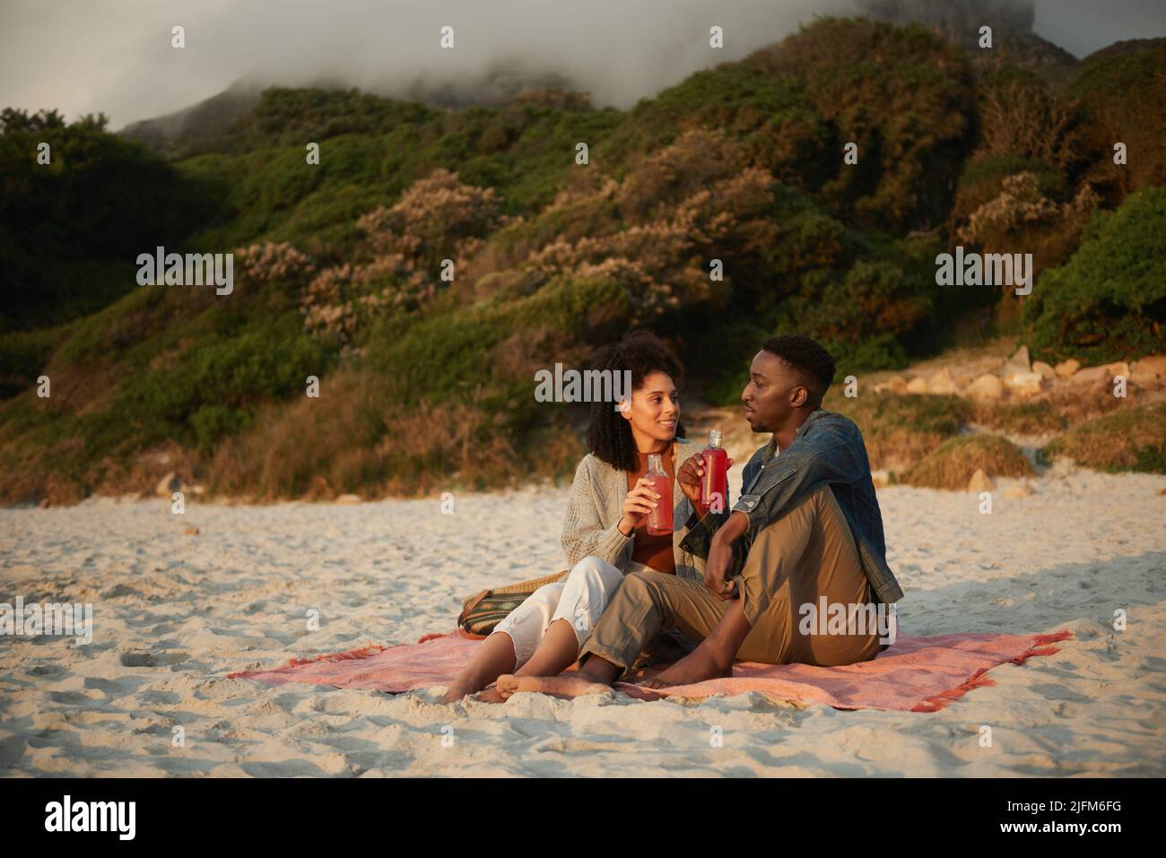 Jeune couple multiethnique souriant parlant sur une plage de sable au coucher du soleil Banque D'Images