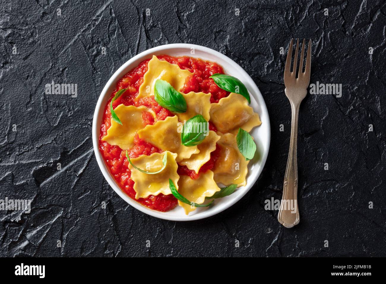 Raviolis à la sauce tomate et feuilles de basilic frais sur une assiette, au-dessus du plat, déposer le grenaille sur fond d'ardoise noire, avec une fourchette Banque D'Images