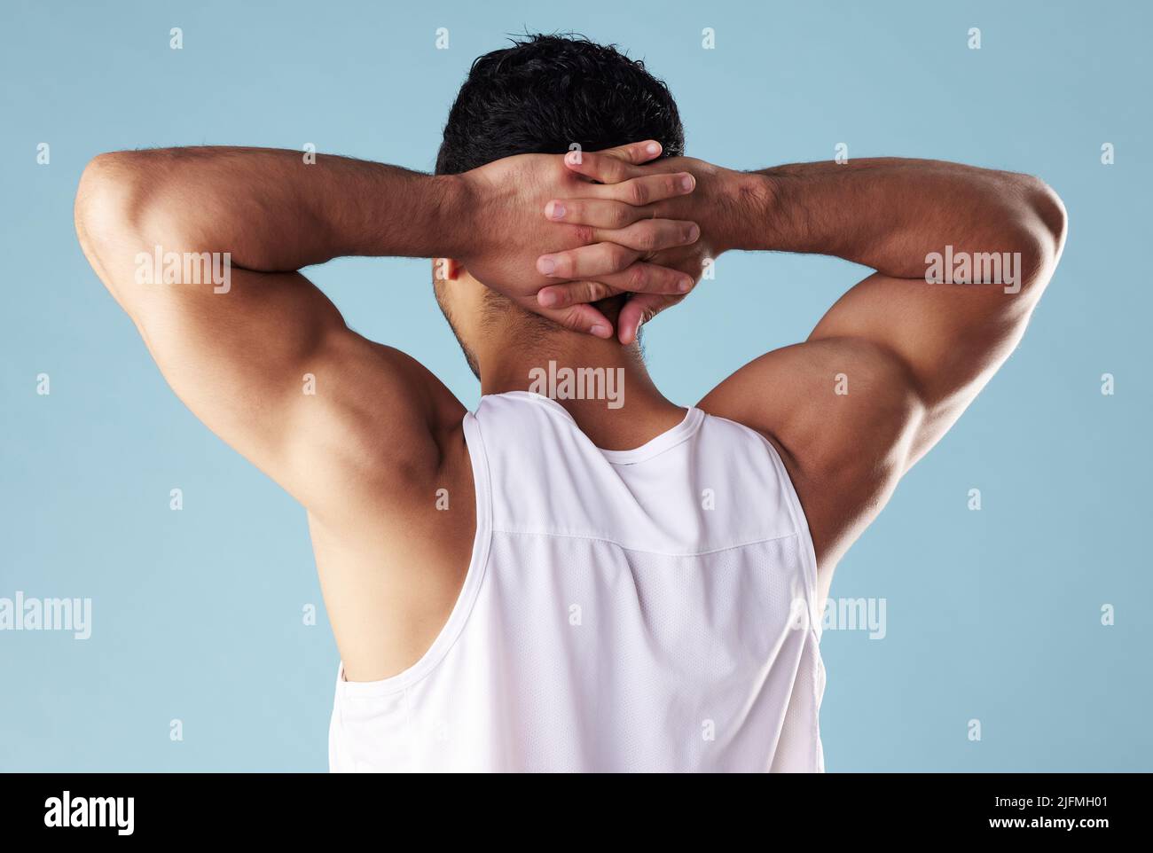 Jeune homme de course mixte, à la vue arrière, portant une veste en studio isolée sur fond bleu. Athlète masculin méconnaissable debout avec les mains derrière lui Banque D'Images