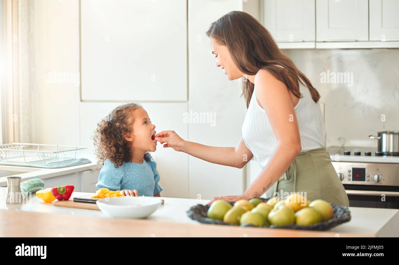 La mère nourrissant les légumes de l'enfant tout en cuisinant ensemble dans la cuisine. Maman et fille passent du temps ensemble à la maison. Les légumes sont bons pour vous Banque D'Images