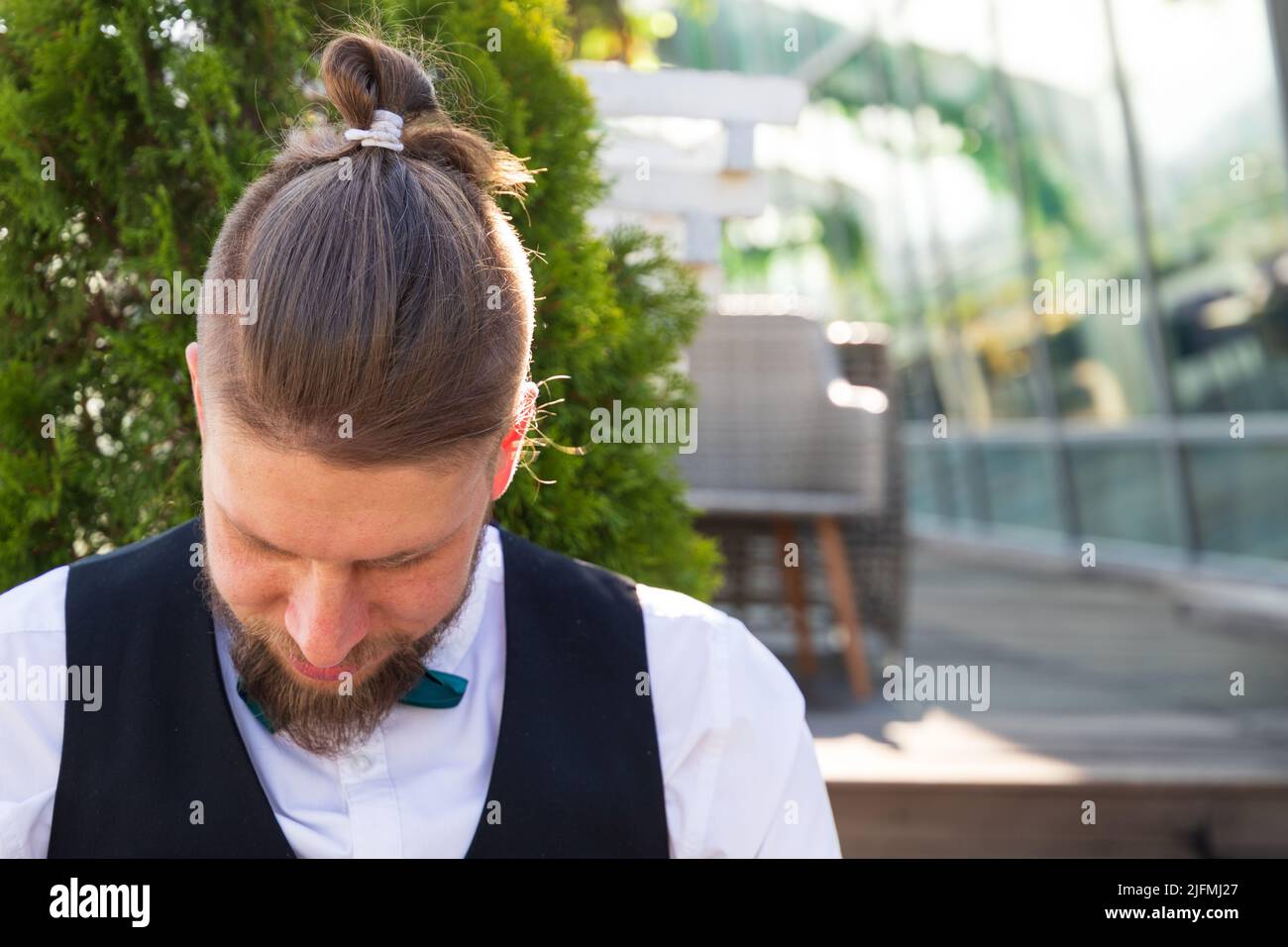 Coupe de cheveux sur un jeune homme barbu dans un costume assis dans un café de rue Banque D'Images