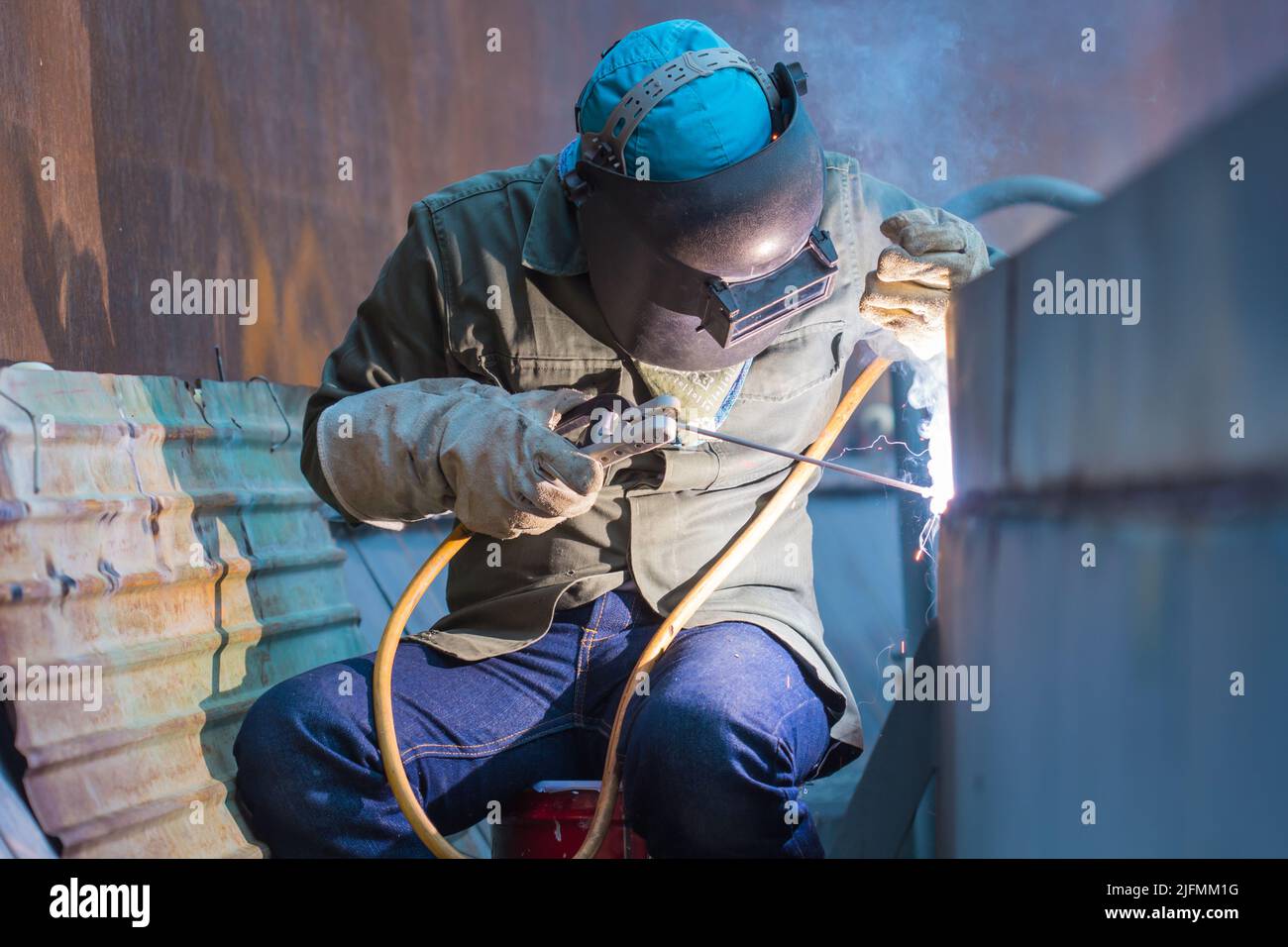 Homme portant des vêtements de protection et répare la plaque de soudage construction industrielle huile et gaz ou réservoir de stockage à l'intérieur d'espaces confinés Banque D'Images