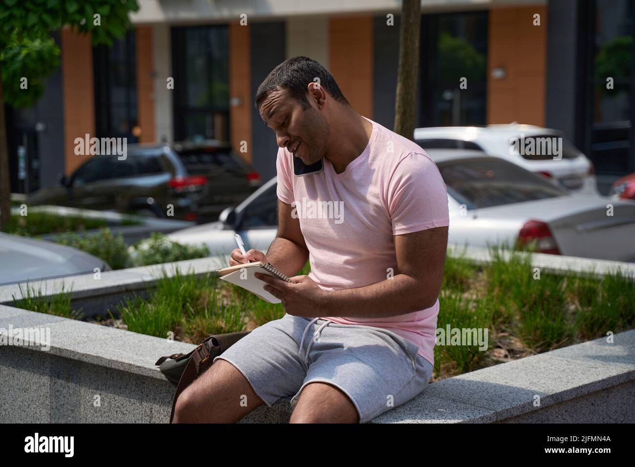 Jeune homme prenant des notes pendant une conversation téléphonique Banque D'Images