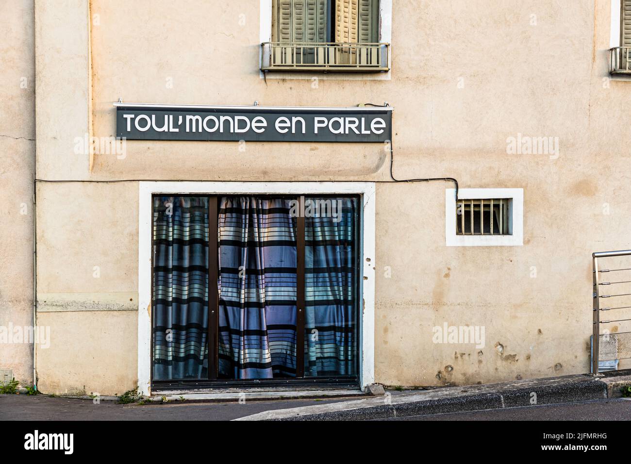 Une enseigne de boutique délabrée portant l'inscription "Toul'monde en parle" – français familier pour "tout le monde en parle", signifiant "tout le monde en parle" – est suspendue au-dessus d'une vitrine masquée par un rideau à Chalon-sur-Saône, en France. Banque D'Images