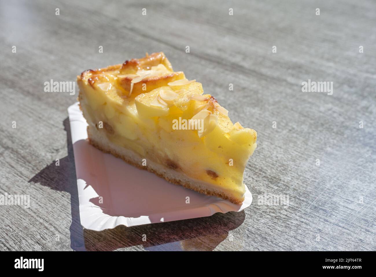 morceau de tarte aux pommes fraîche avec amandes sur un carton sur une table au soleil, délicieux dessert d'été, espace de copie, foyer sélectionné, profondeur de fiel étroite Banque D'Images
