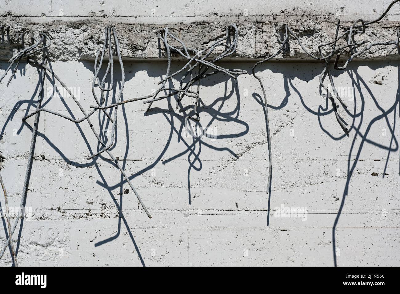 les barres de renfort après démolition s'accrocheraient inutiles à un mur en béton brillant et jeaient des ombres, un arrière-plan abstrait de grunge pour l'architecture et le bâtiment Banque D'Images