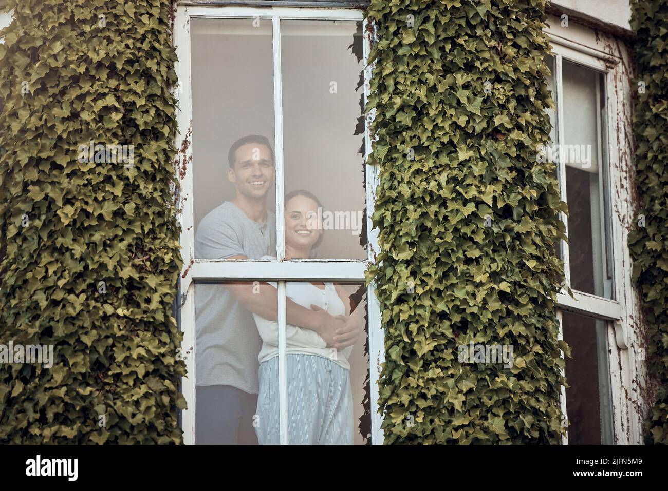 Heureux jeune couple mixte de course debout dans leur fenêtre. Couple aimant se liant et passer du temps ensemble à la maison. Amoureux debout près d'une fenêtre avec Banque D'Images