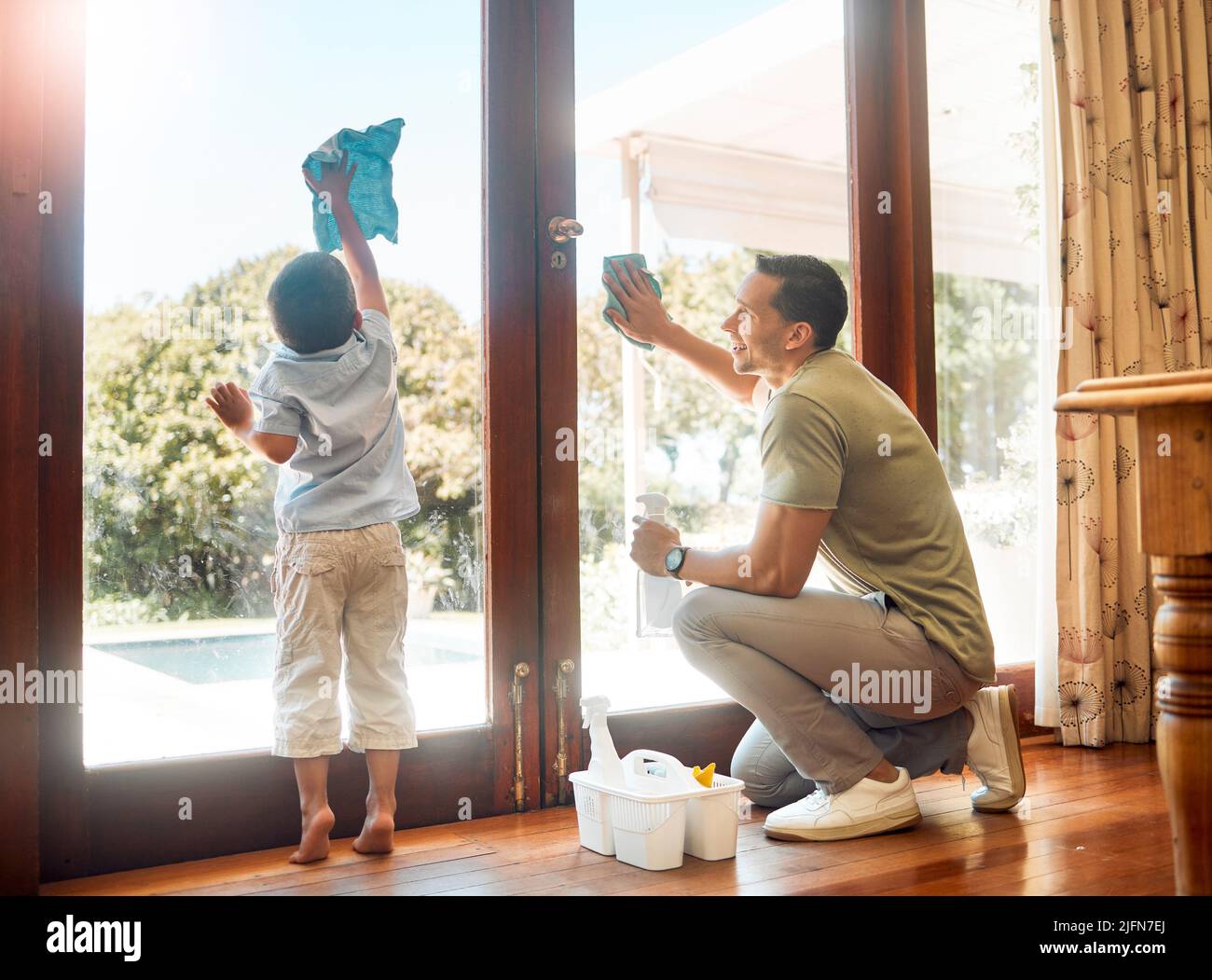 Un petit garçon aidant son père à laver et à essuyer les portes en verre propres pour les tâches ménagères à la maison. Père et fils heureux faisant le nettoyage de printemps ensemble. Enfant Banque D'Images