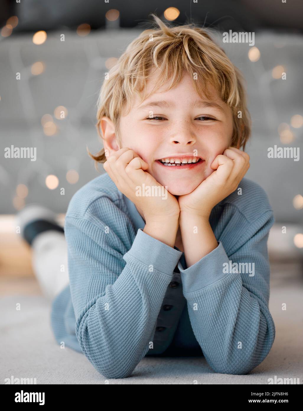 Portrait d'un petit garçon blanc souriant allongé sur le sol avec sa tête reposant dans les mains à la maison. Le visage d'un adorable gamin joyeux Banque D'Images
