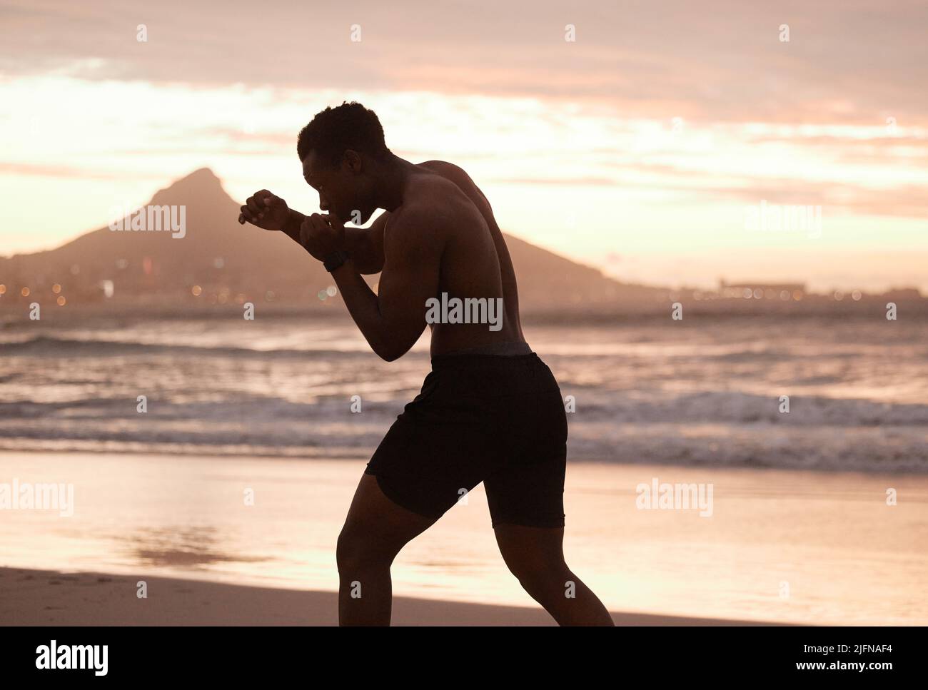 Un africain américain pratiquant la boxe dans l'ombre sur une plage au coucher du soleil. L'homme noir se concentre sur la vitesse, la force et la forme physique tout en montrant sa musculature Banque D'Images