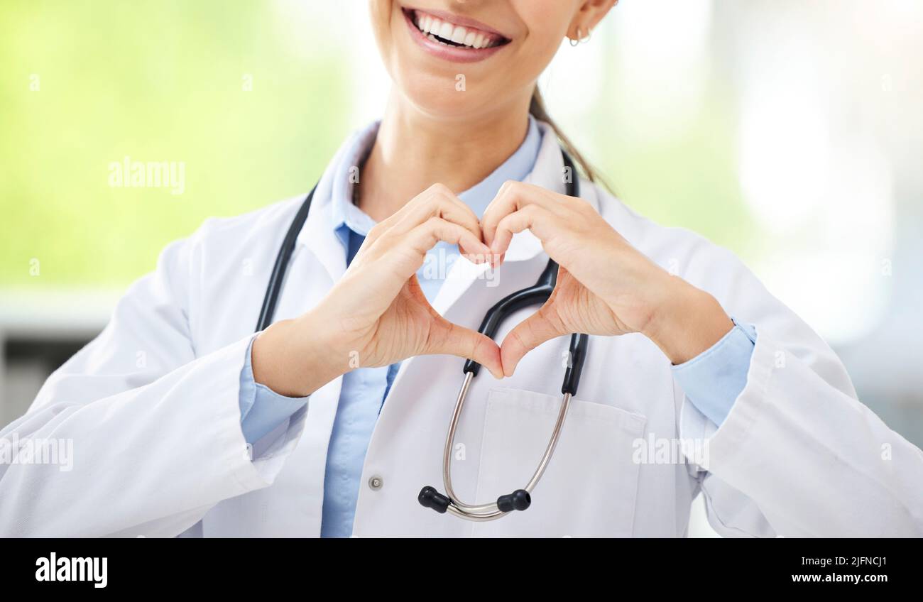 Femme inconnue médecin de race mixte assis dans son bureau et montrant un geste de forme de coeur avec sa main dans un hôpital. Une femme hispanique fait la main Banque D'Images