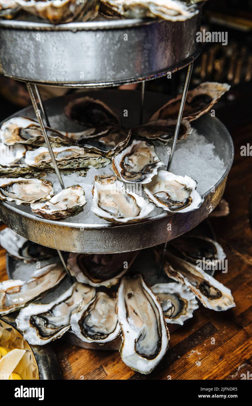 Huîtres ouvertes sur une assiette blanche avec citron sur fond de bois foncé, fruits de mer, mollusque, luxe. Banque D'Images