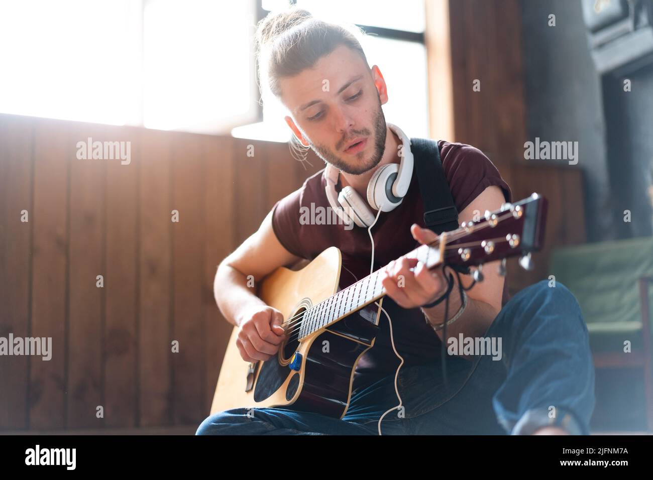 Beau jeune homme jouant de la guitare acoustique assis plancher salon loft pièce caucasien mâle casque hippster guitariste pratiquant le chant appréciez mus Banque D'Images