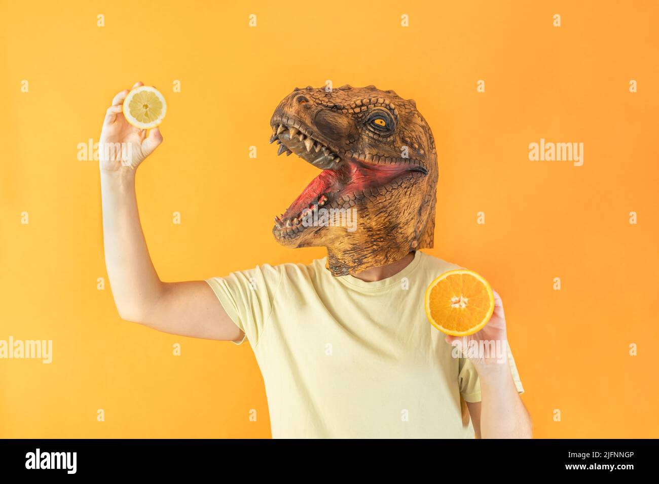 Femme portant un masque de tête d'animal surréaliste tenant des tranches fraîches de citron et d'orange, isolé sur fond orange avec espace de copie Banque D'Images