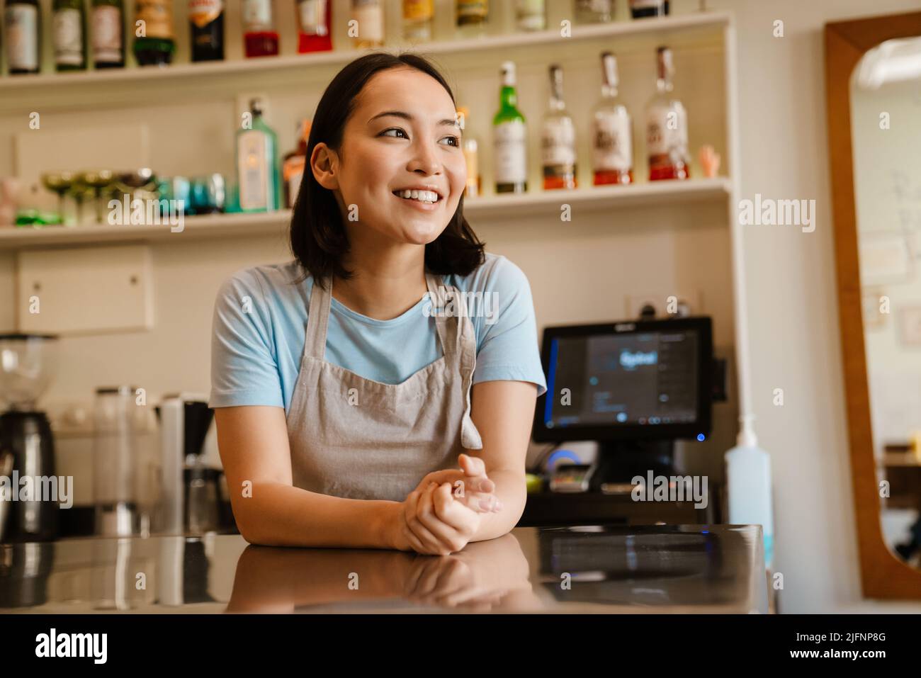 Une jeune serveuse asiatique porte un tablier souriant alors qu'elle travaille dans un café Banque D'Images