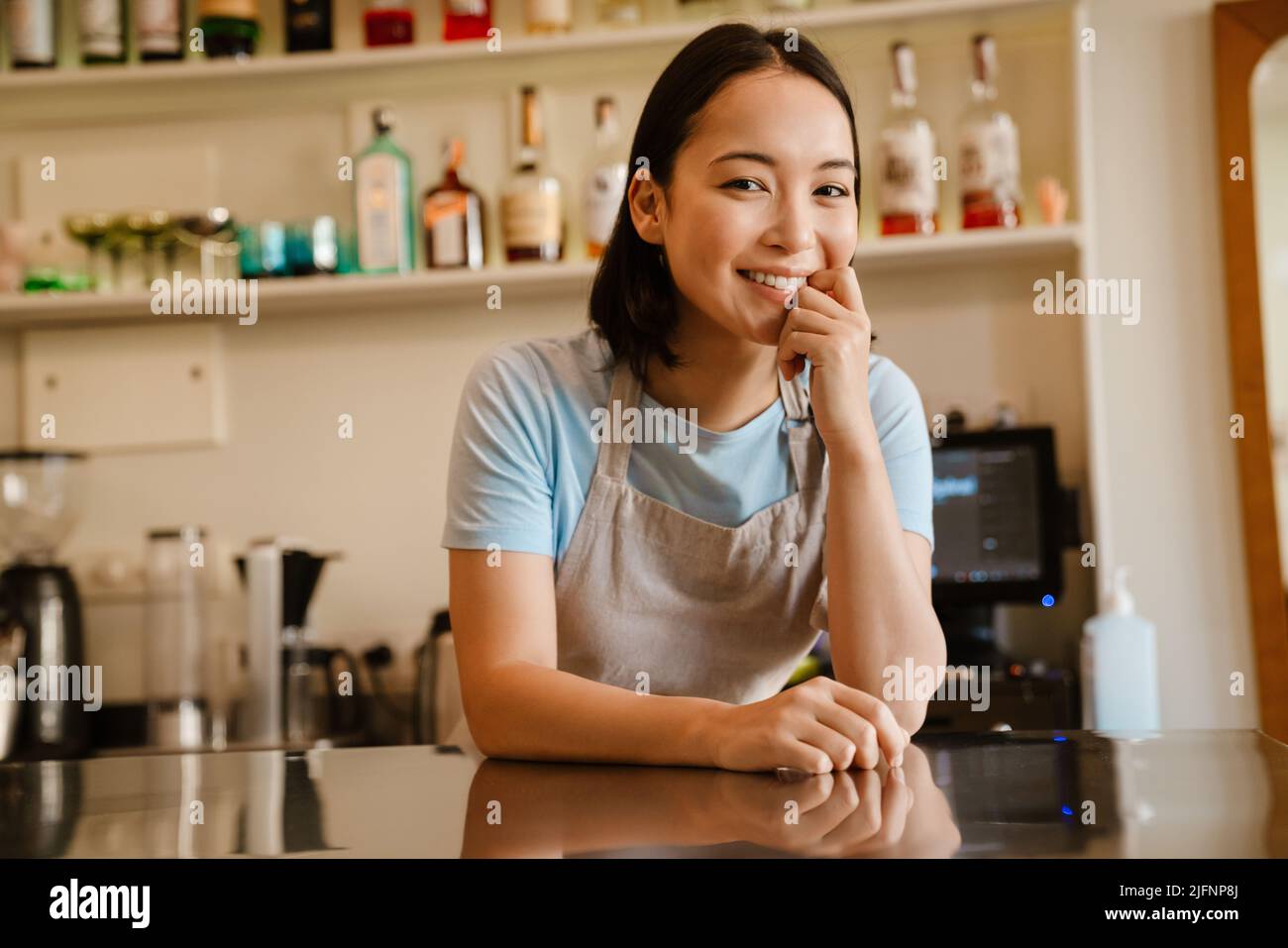 Une jeune serveuse asiatique porte un tablier souriant alors qu'elle travaille dans un café Banque D'Images