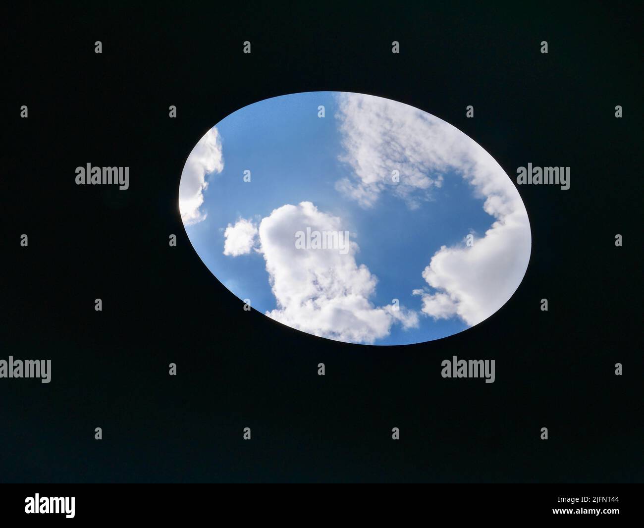 Ciel bleu avec nuages vus à travers trou ovale. Banque D'Images