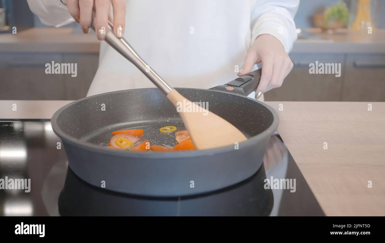 Gros plan de la femme cuisant dans une nouvelle poêle à frire. Action. Rôtir des légumes sur un nouveau modèle moderne de poêle à frire. Cuisiner des aliments sains dans une nouvelle poêle Banque D'Images