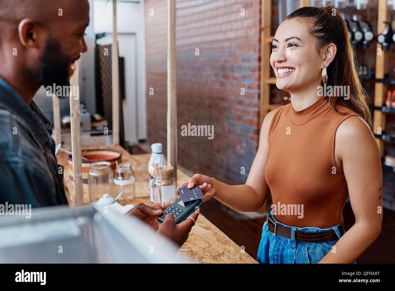 Un client hispanique heureux qui paie un repas dans un restaurant à l'aide d'une machine nfc et d'une carte de crédit. Jeune femme souriante faisant un achat dans un magasin avec Banque D'Images