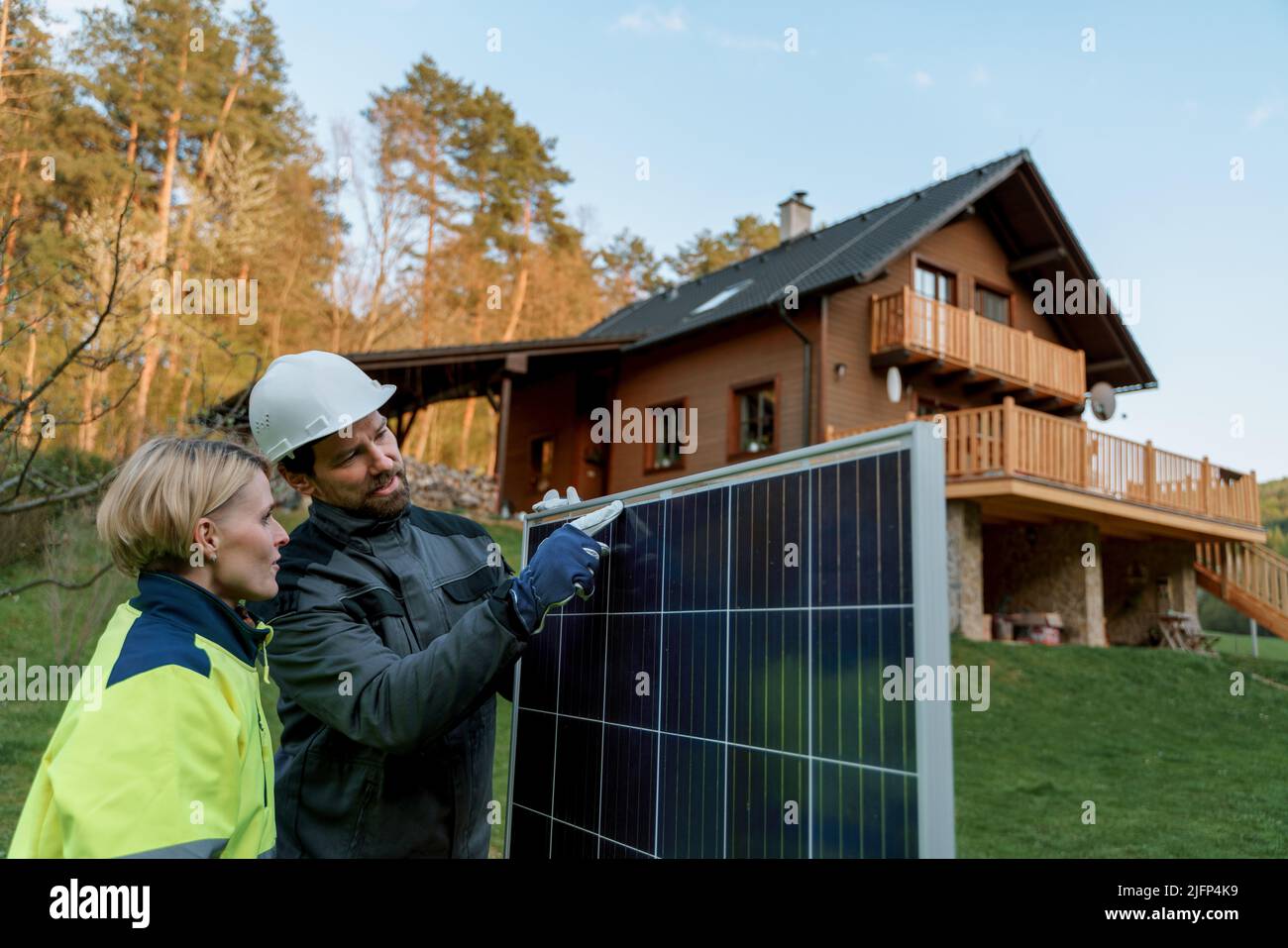 Homme et femme installateurs solaires transportant le module solaire tout en installant le système de panneaux solaires dans la maison. Banque D'Images