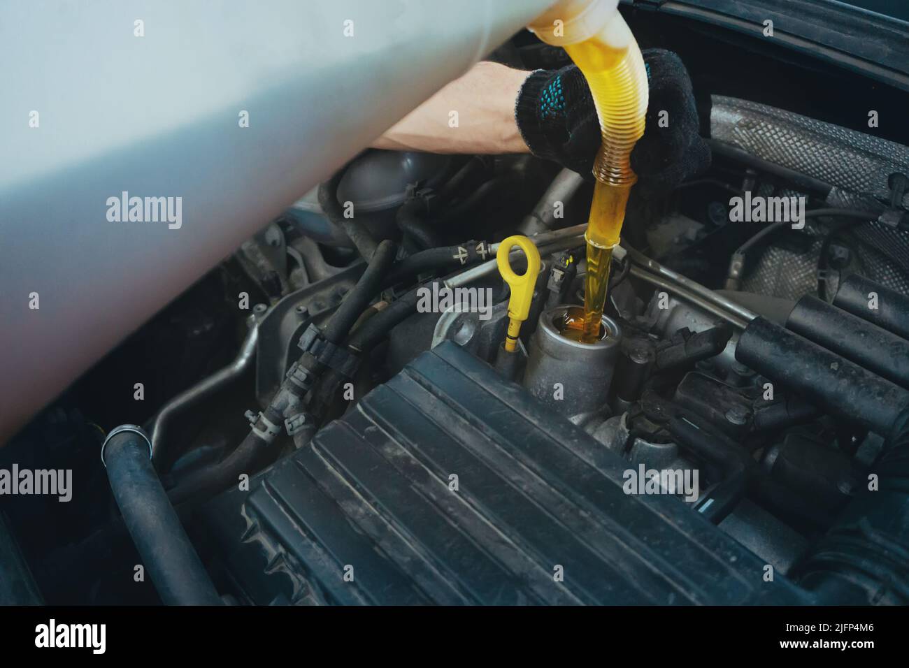 Un technicien de maintenance verse de l'huile moteur dans le moteur dans le garage d'entretien de la voiture, en gros plan. Banque D'Images