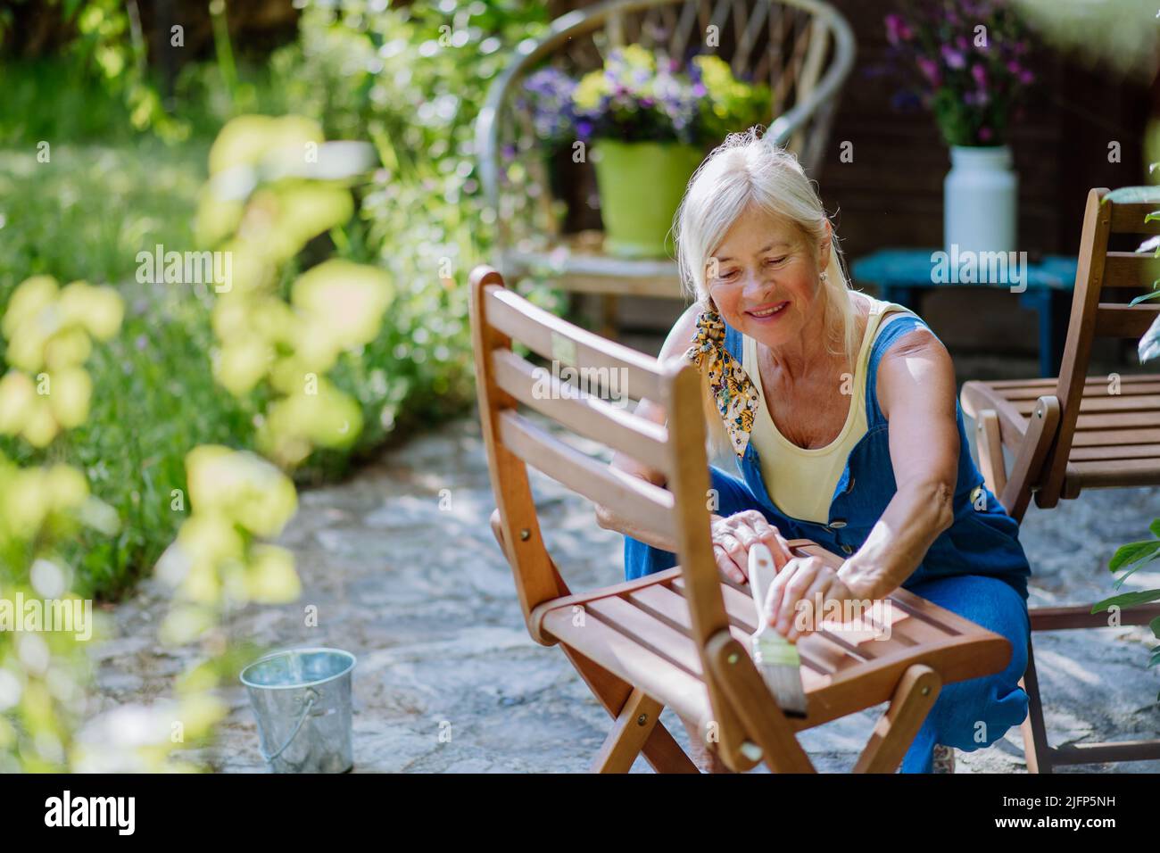 Femme âgée qui nettoie et rénove les meubles de jardin et prépare le jardin pour l'été Banque D'Images