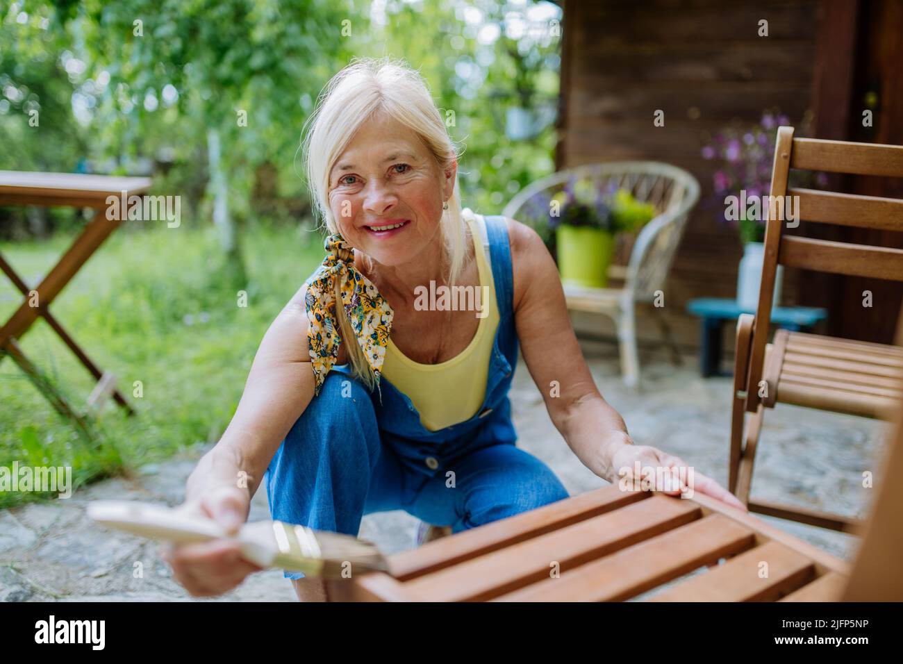 Femme âgée qui nettoie et rénove les meubles de jardin et prépare le jardin pour l'été Banque D'Images