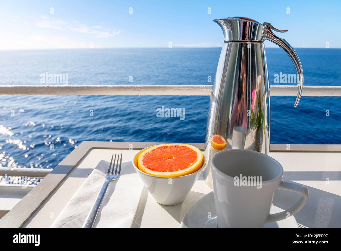 Une carafe de café à côté d'un pamplemousse coupé sur un balcon avec vue sur l'océan d'un bateau de croisière en mer, un jour d'été. Banque D'Images