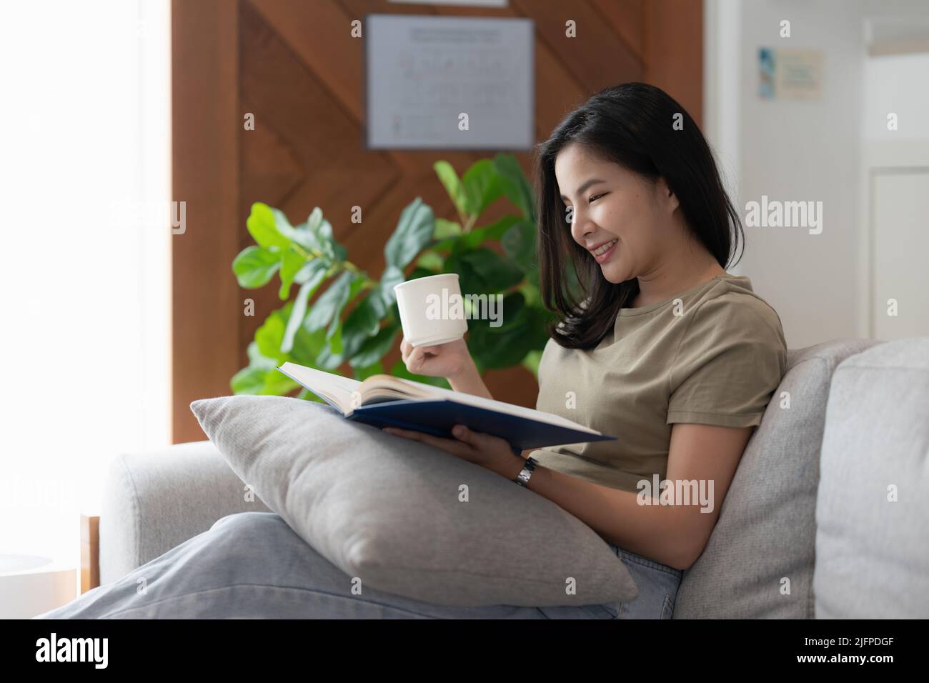Image d'une jeune femme asiatique lisant un livre assis sur un canapé. Concept de style de vie et de détente. Banque D'Images
