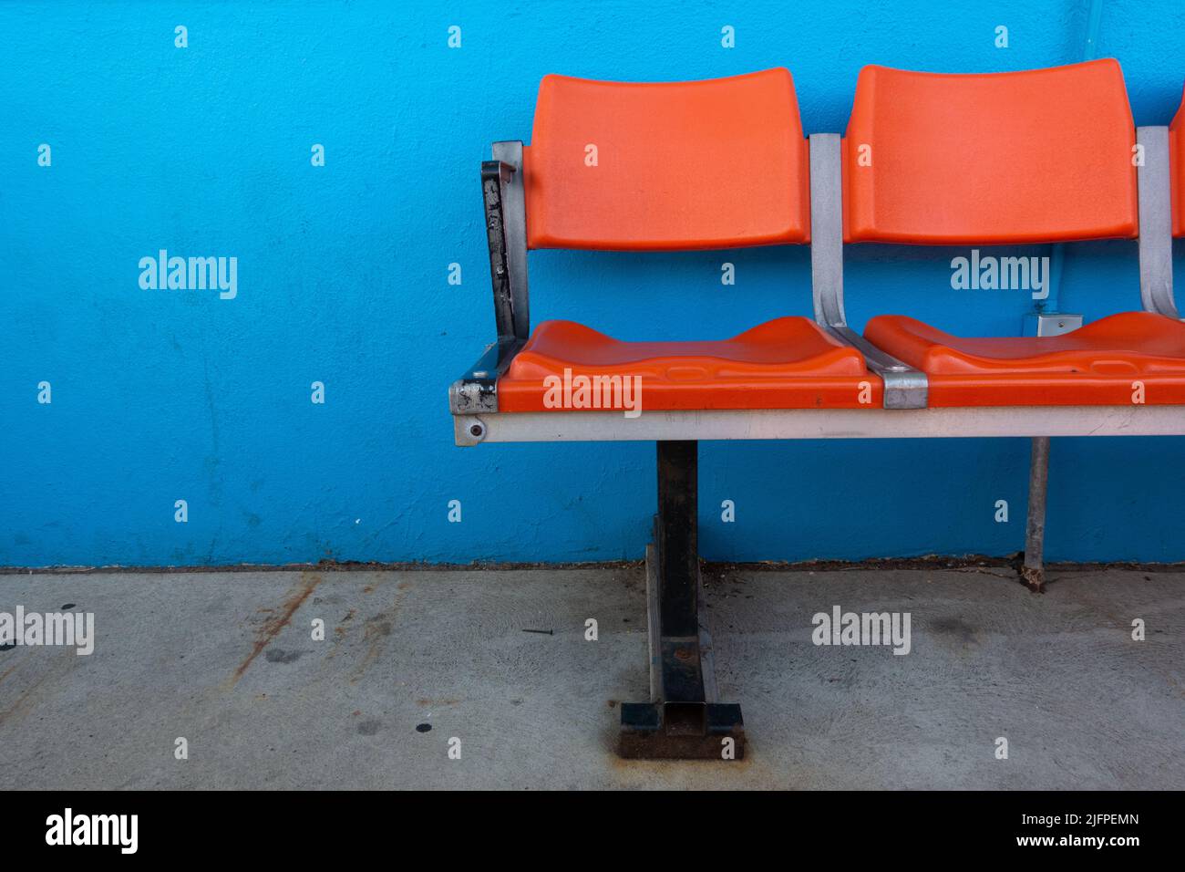 Rangée de sièges de stade en plastique orange vides contre un mur peint bleu vif sur un sol en béton Banque D'Images