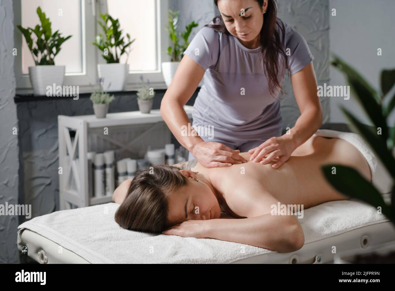 Femme caucasienne ayant un traitement de massage en clinique de thérapie. Massage de dos d'huile, concept de spa et de soins de santé. Soulagement de la douleur. Physiothérapeute dans vert moderne Banque D'Images