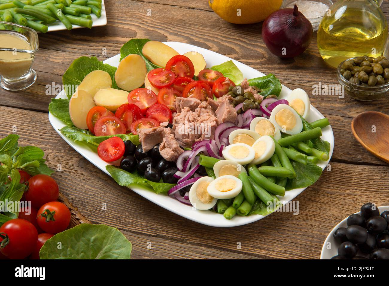 Salade Niçoise traditionnelle dans un saladier blanc rectangulaire sur une table rurale ancienne avec sauce et ingrédients. Mise au point sélectionnée. Banque D'Images