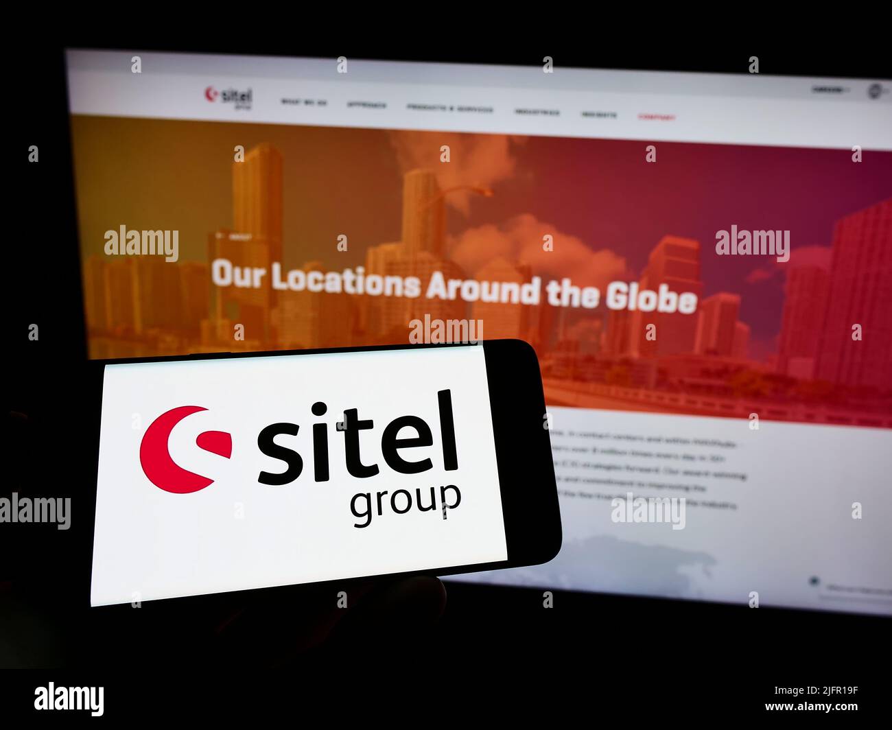 Personne tenant un téléphone portable avec le logo de la société américaine de centre de contact Sitel Group sur l'écran en face de la page Web d'affaires. Mise au point sur l'affichage du téléphone. Banque D'Images